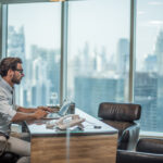 Businessman using laptop at desk with window view of city, Dubai, United Arab Emirates